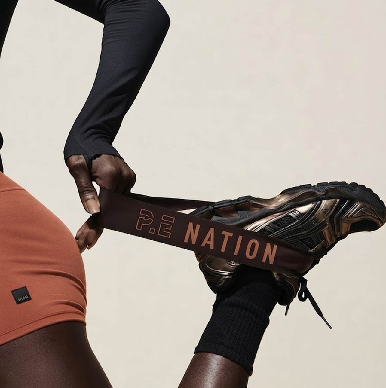 Un athlète de dos noue une corde de course portant une chaussure de sport, avec un fond neutre.