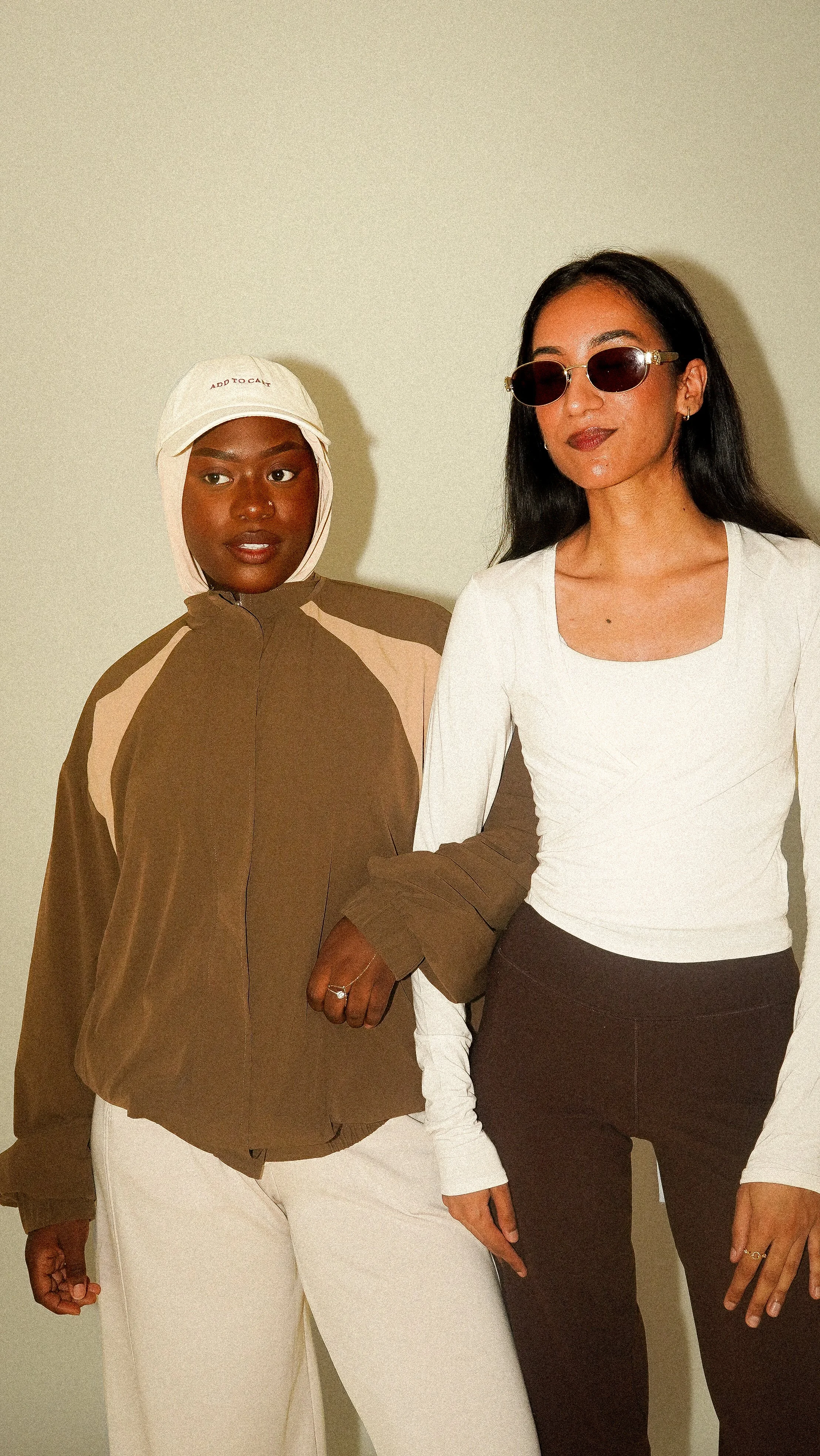 Deux femmes debout côte à côte, tenant la main, dans une pièce avec un mur beige.