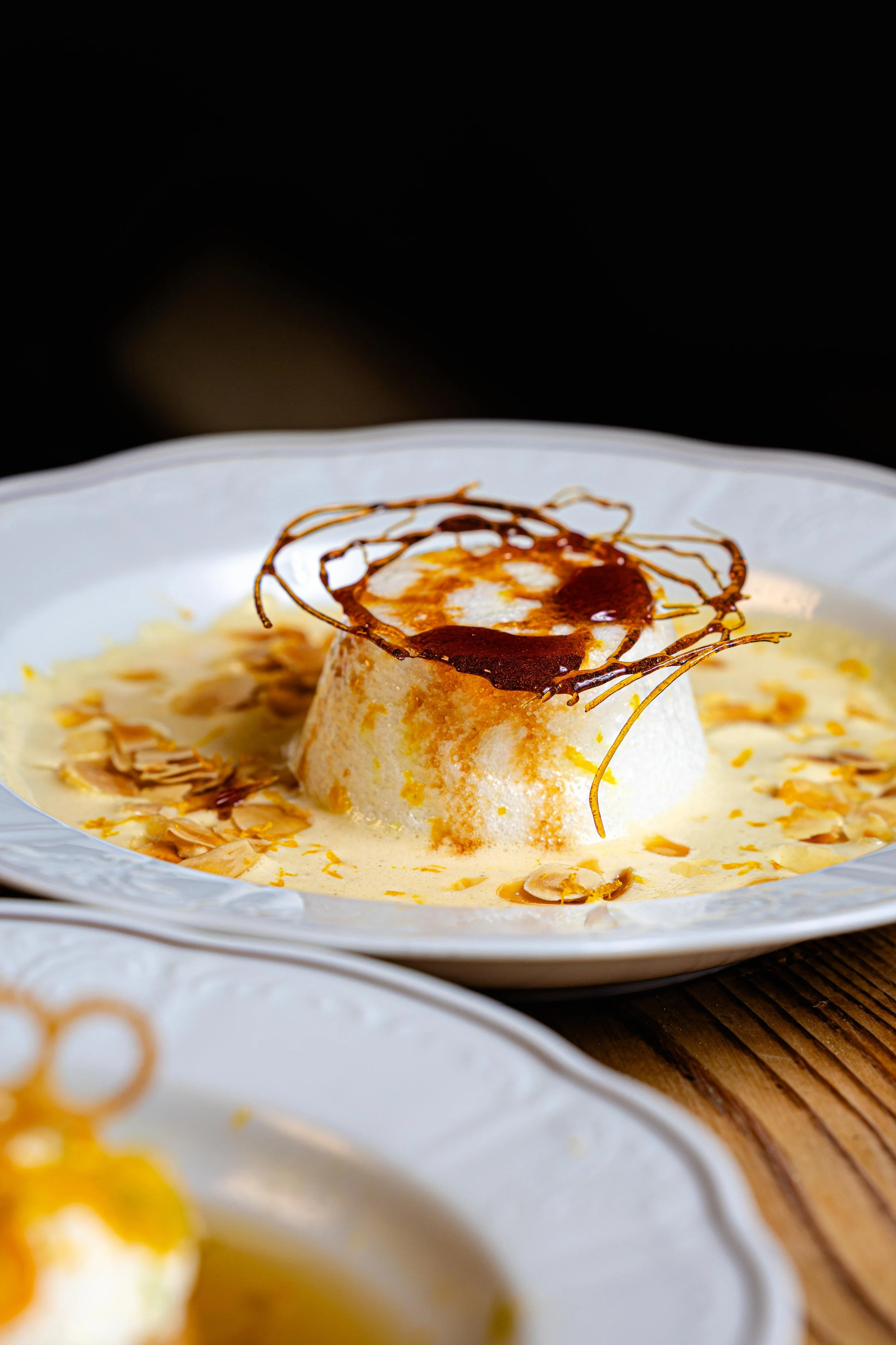 Dessert gourmand avec une quenelle de glace à la vanille, garnie de sauce au chocolat, de morceaux de chocolat et d'amandes effilées, servi dans une assiette blanche.
