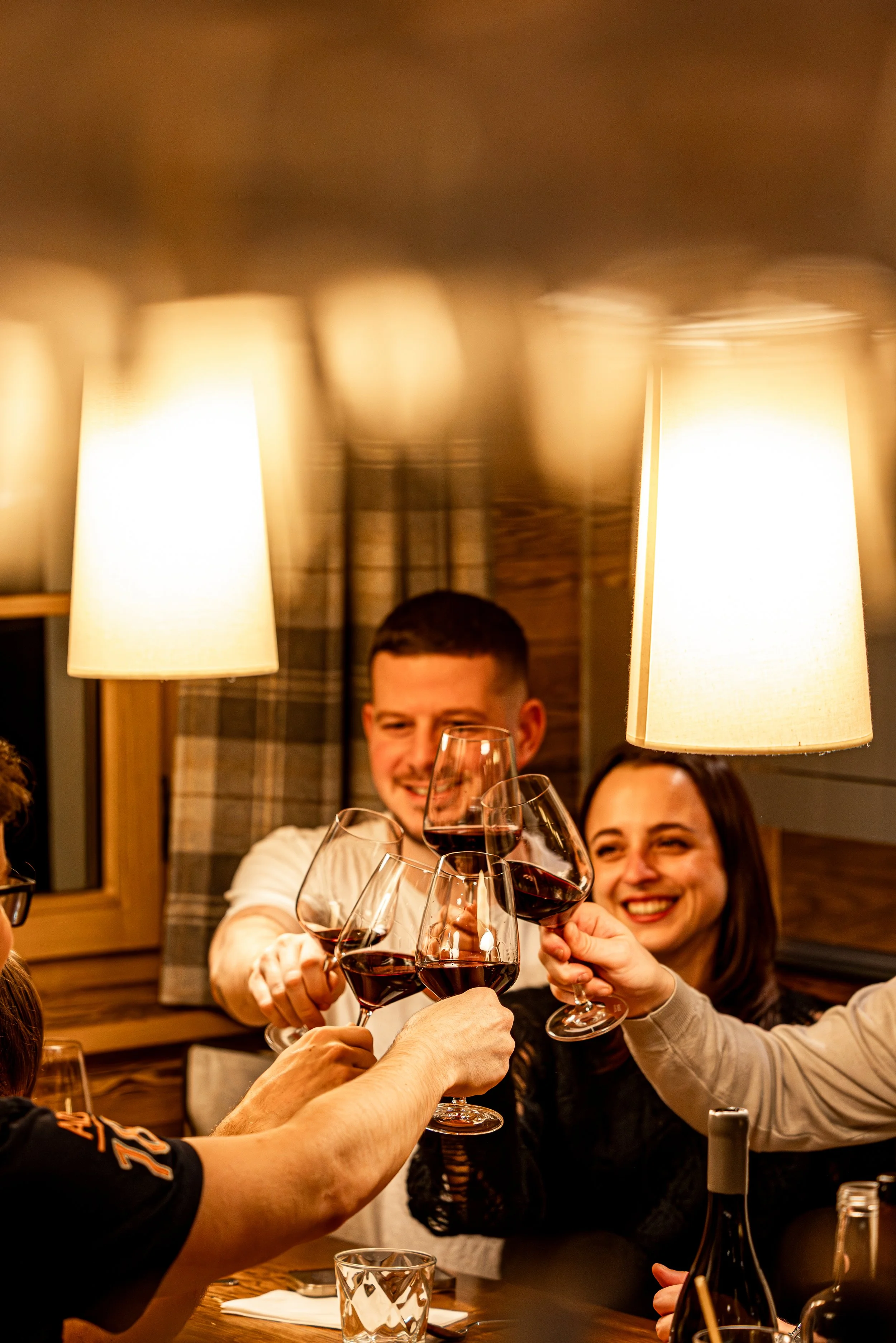 Groupe de personnes faisant un toast avec du vin rouge dans un restaurant chaleureux.