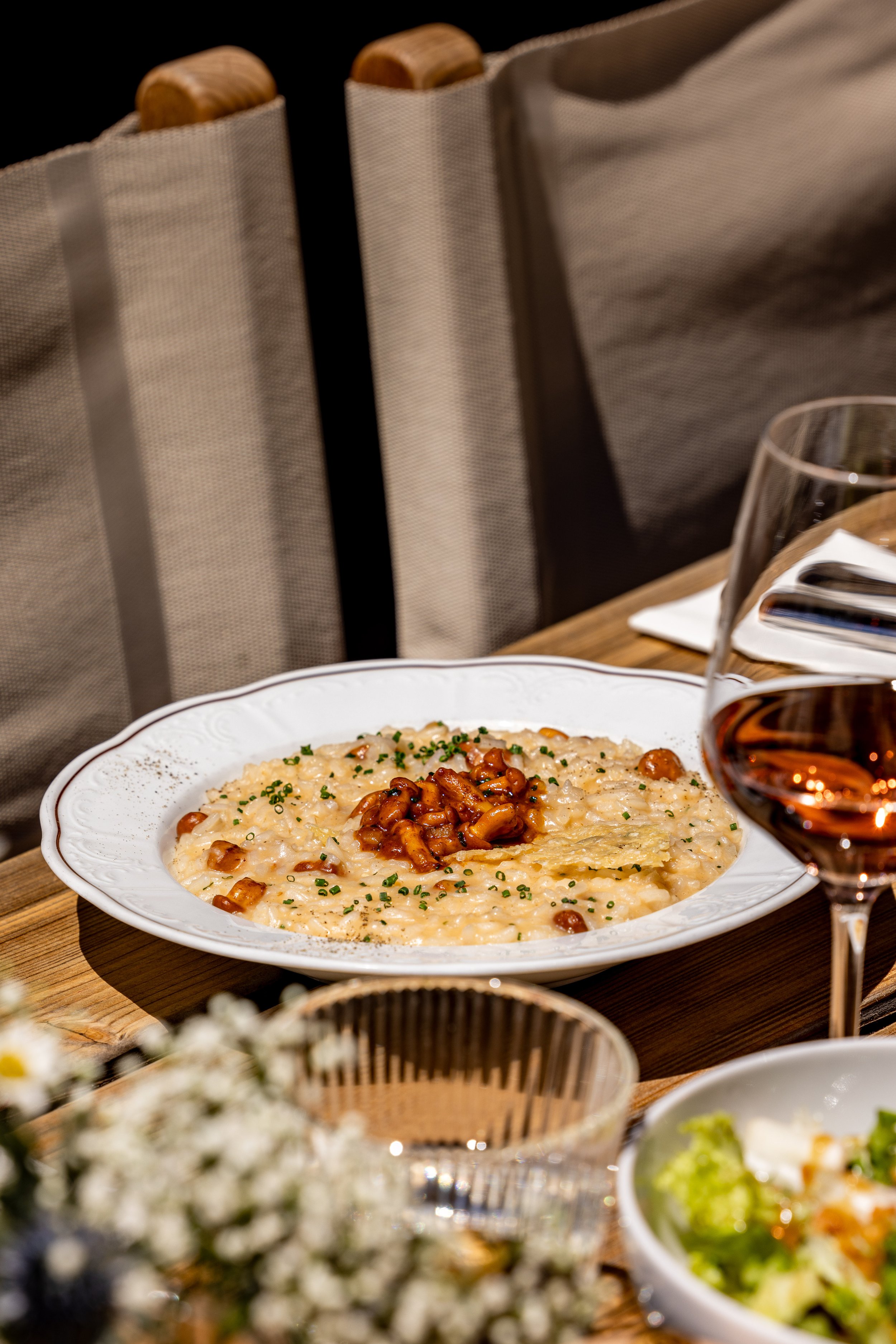 Plat de risotto garni de haricots et de persil, avec un verre de vin rouge à côté, sur une table en bois. En arrière-plan, des sacs en toile beige et un autre plat de salade.