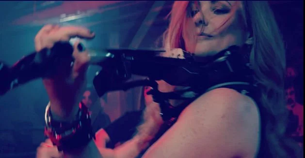 Une femme avec des cheveux colorés joue du violon dans une ambiance sombre et colorée.