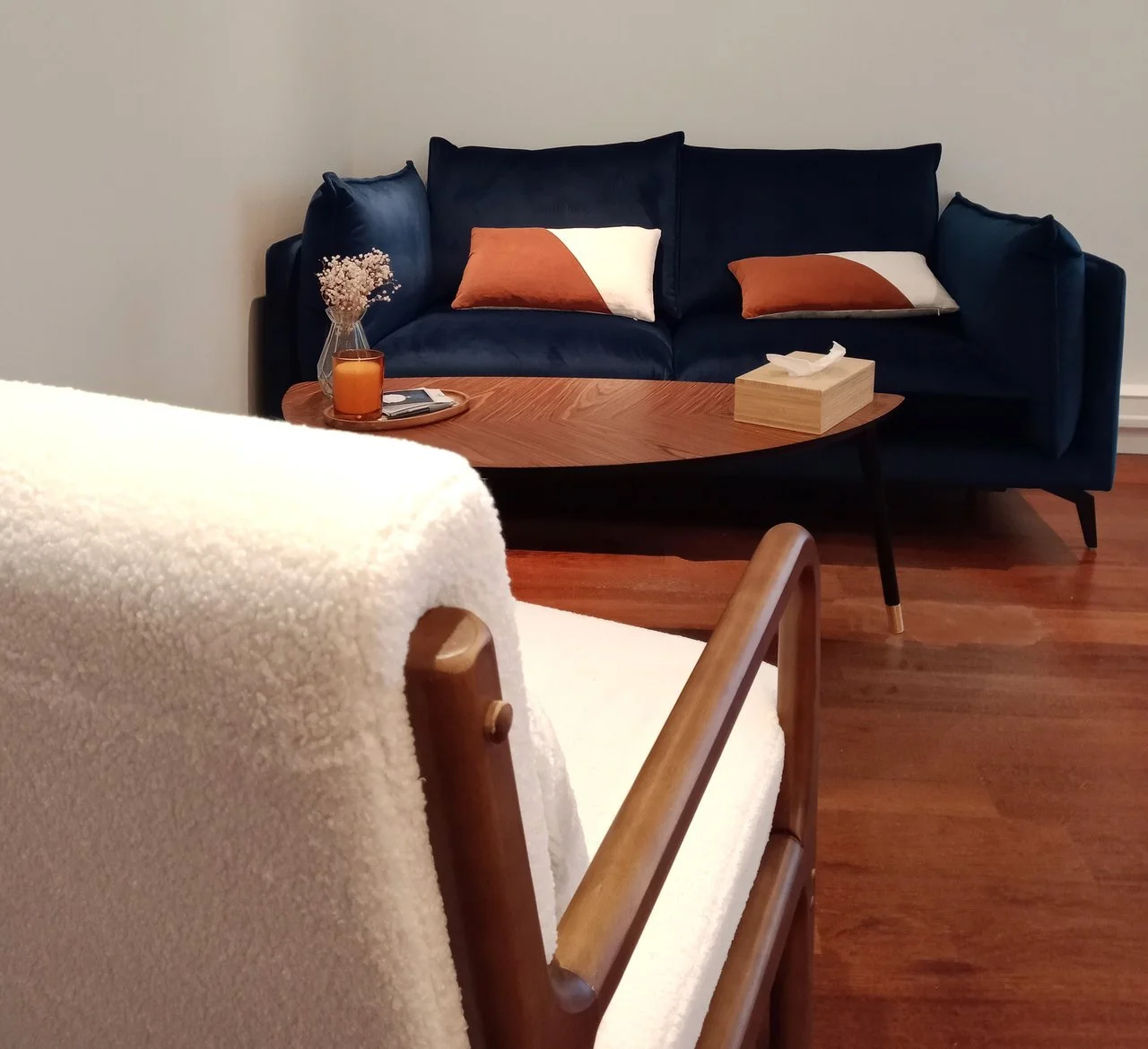 Un salon avec un canapé bleu foncé, un tapis en bois, une table avec une bougie, un vase avec des fleurs séchées, des mouchoirs en boîtier en bois, et des coussins décoratifs.