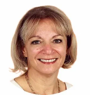 Close-up portrait of a smiling middle-aged woman with shoulder-length blonde hair, wearing a white top and a gold necklace.