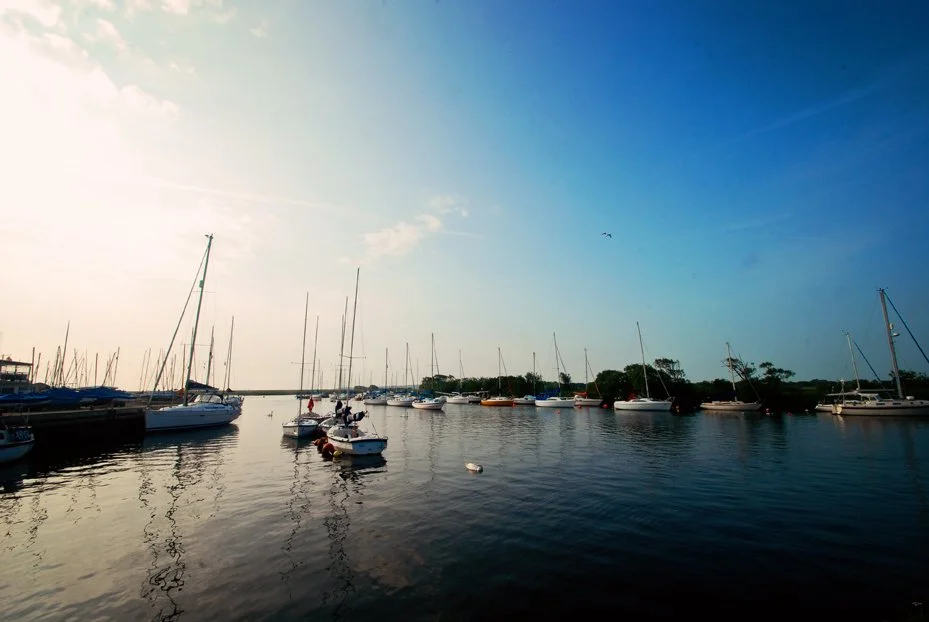 Sailboats docked at a marina under a partly cloudy sky during daytime.