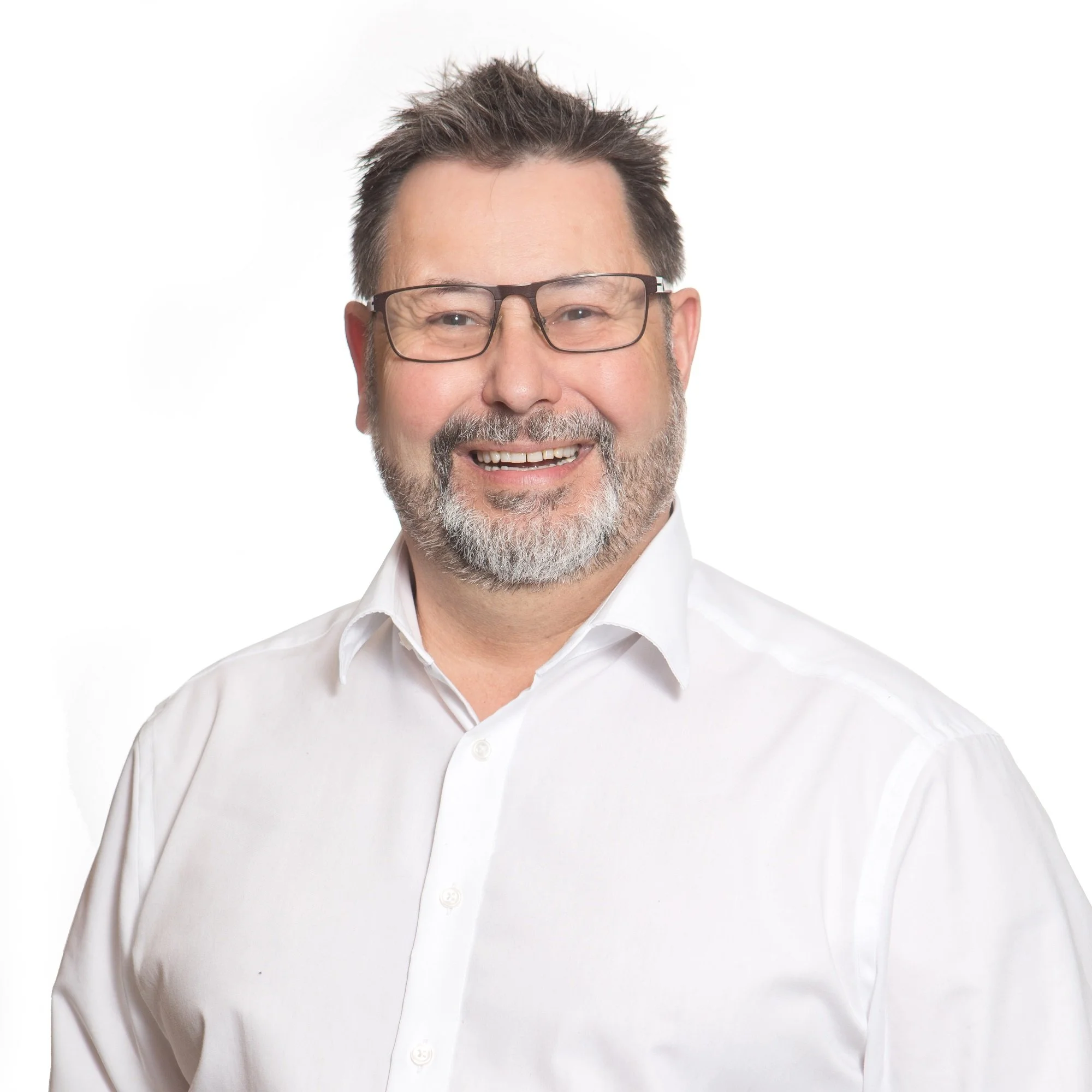 Close-up of a smiling middle-aged man with glasses, short brown hair, and a salt-and-pepper beard wearing a white shirt against a white background.