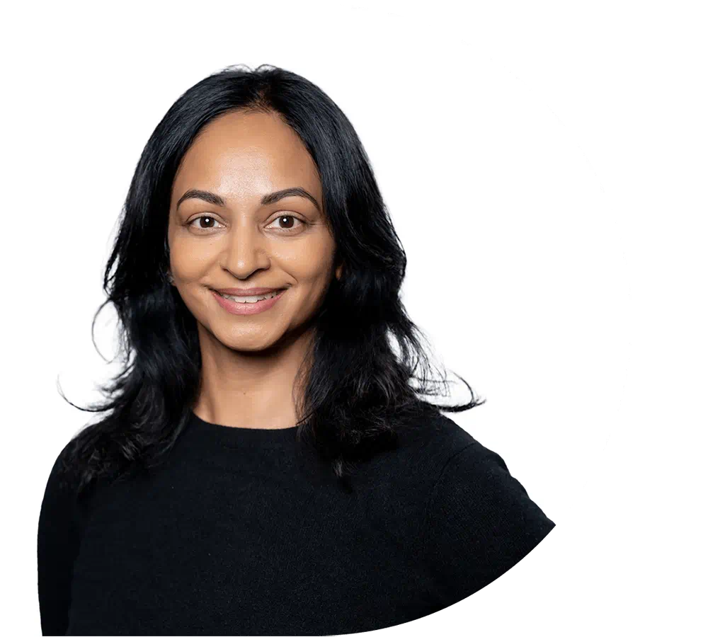 A smiling woman with shoulder-length black hair wearing a black top, looking directly at the camera against a plain white background.