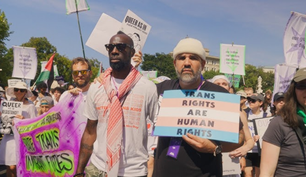 People participating in a pride march holding signs and banners supporting transgender and LGBTQ rights.