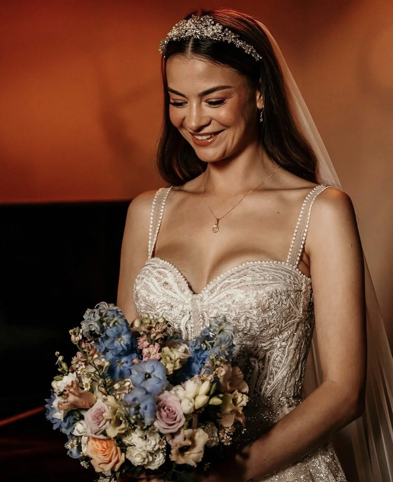 A woman in a wedding dress holding a bouquet of flowers, smiling, with a pearl headband and veil.