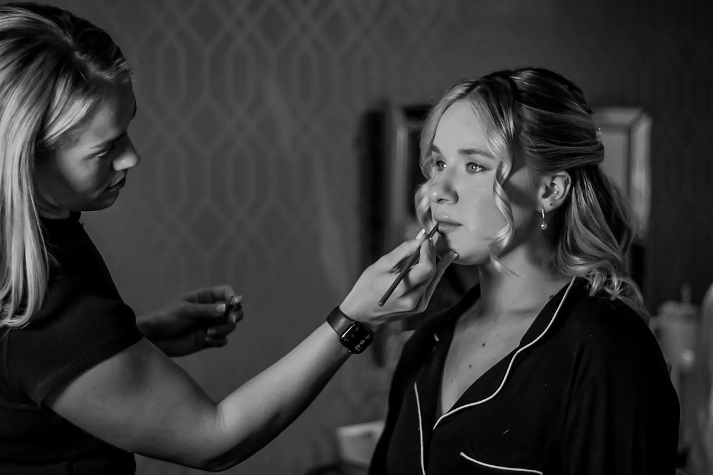A woman with blonde hair having her makeup applied by a makeup artist at a beauty salon.