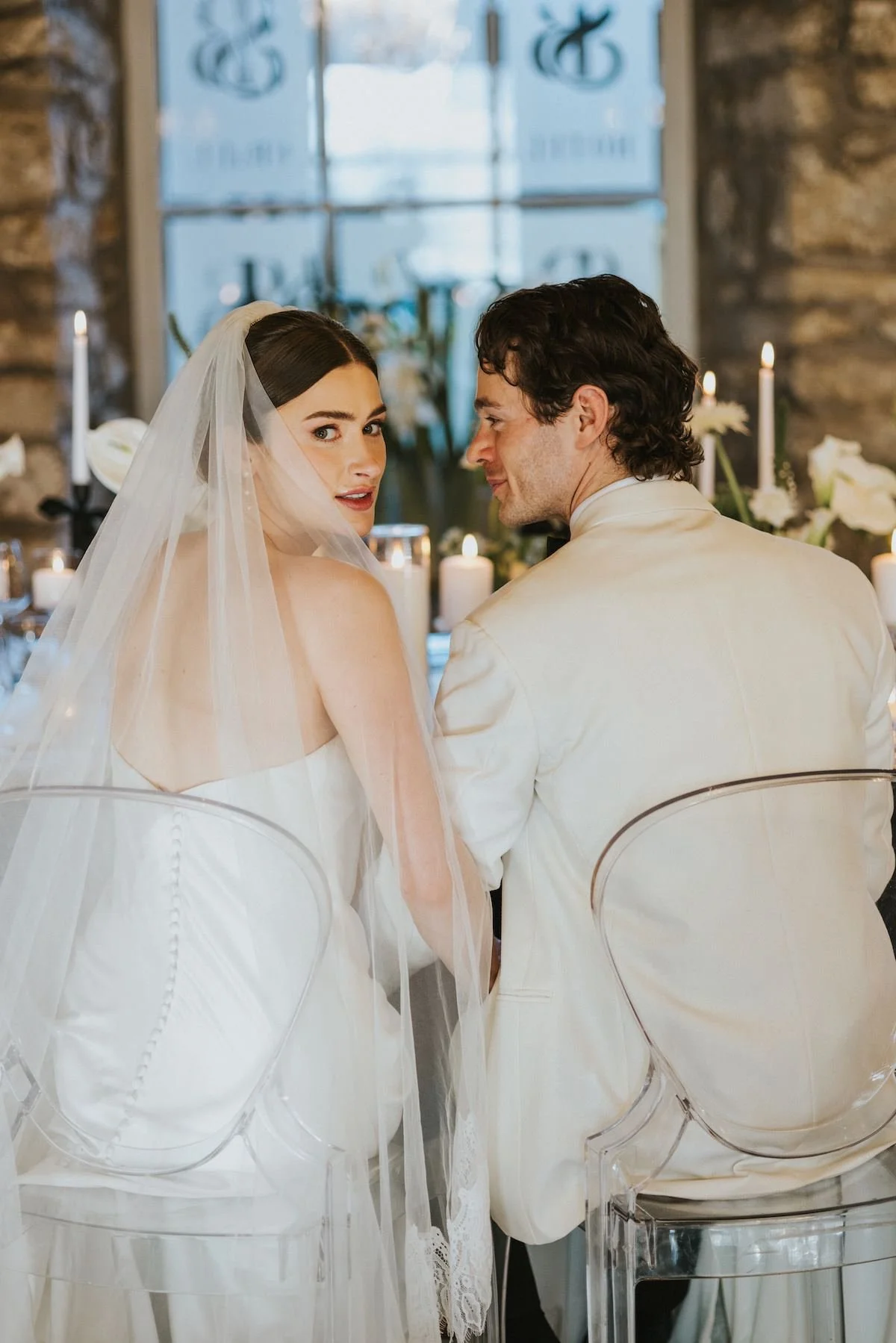 A bride and groom sitting close together at their wedding reception, with candles and floral arrangements in the background.