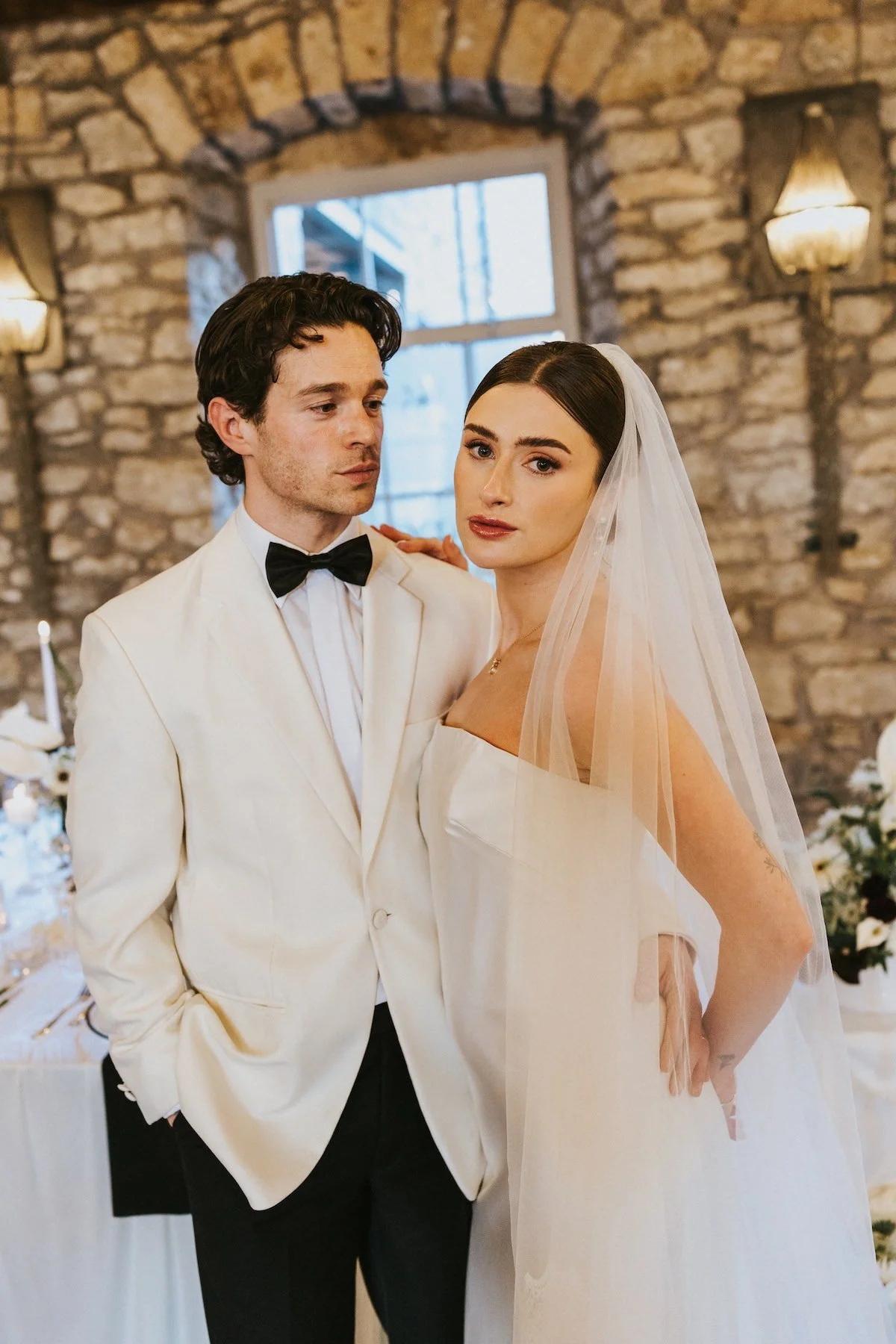 The bride is wearing a strapless wedding dress with a veil and has dark hair and makeup.
