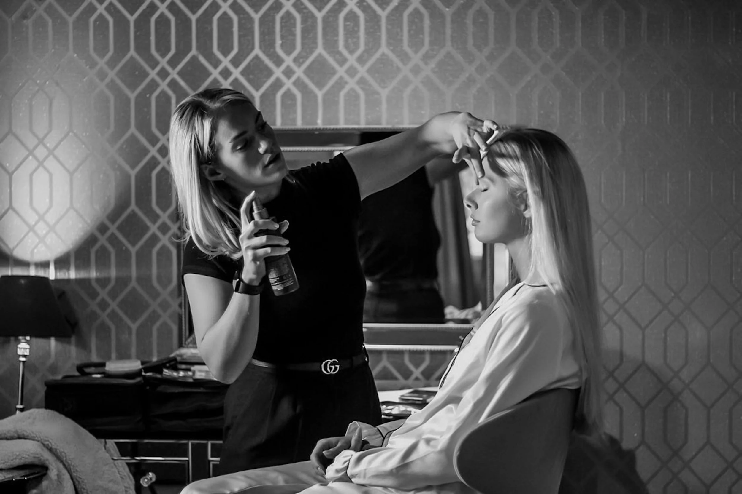 A hairstylist applies hairspray to a woman's hair in a modern salon.