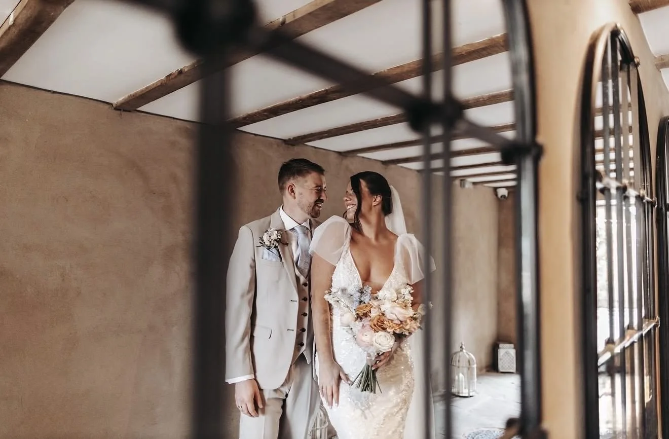 A bride and groom smiling at each other during their wedding photos in an indoor setting.