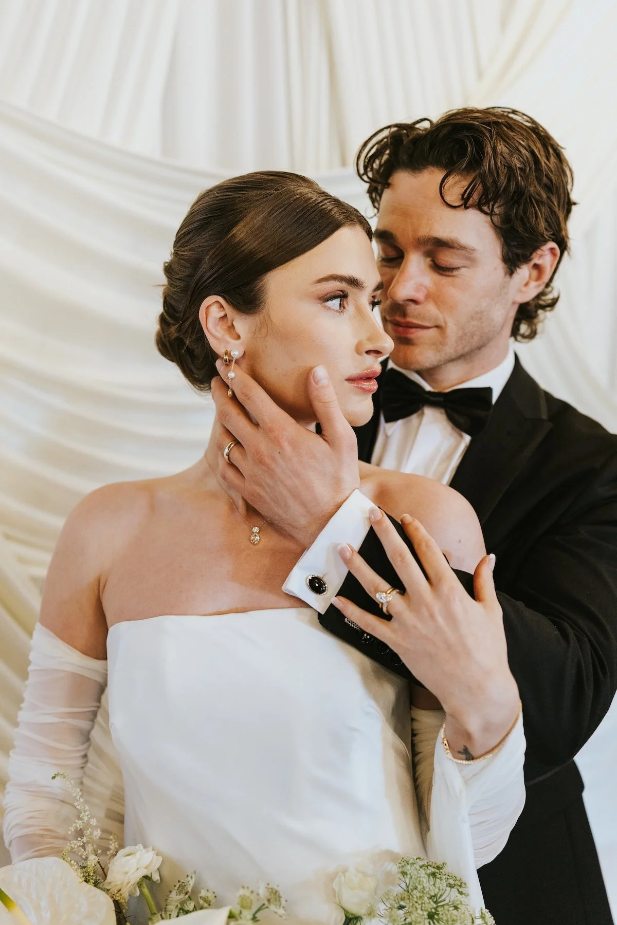 A bride and groom sharing an intimate moment at their wedding, with the groom gently holding the bride's face and the bride looking at him, surrounded by white floral decor.