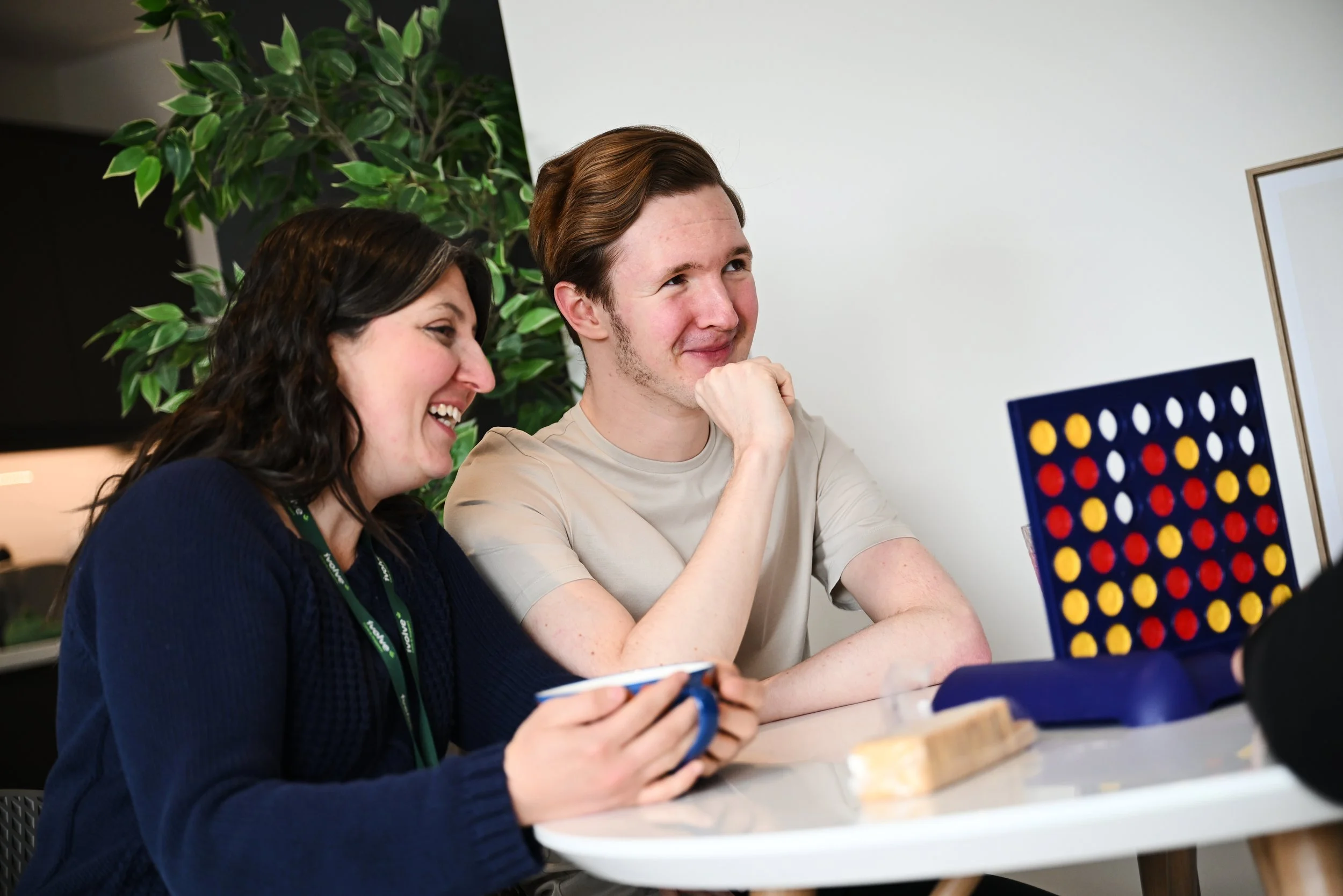 Two people, a woman and a man, playing Connect Four at a table, smiling and laughing.