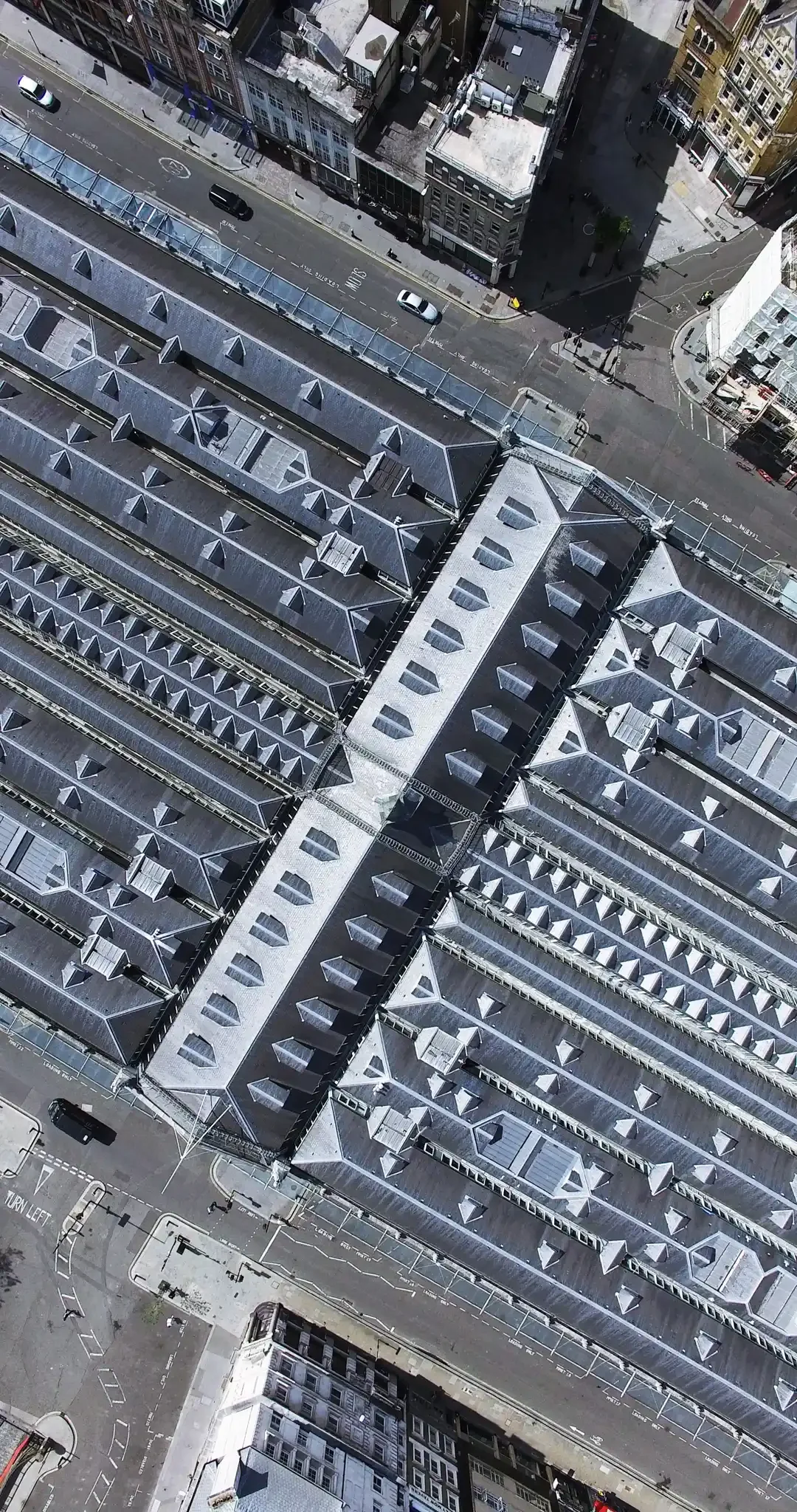 Bird's eye view of Smithfield Market, an abstract architectural view, with a city street with parked cars, buildings, and an adjacent rooftop with multiple skylights.