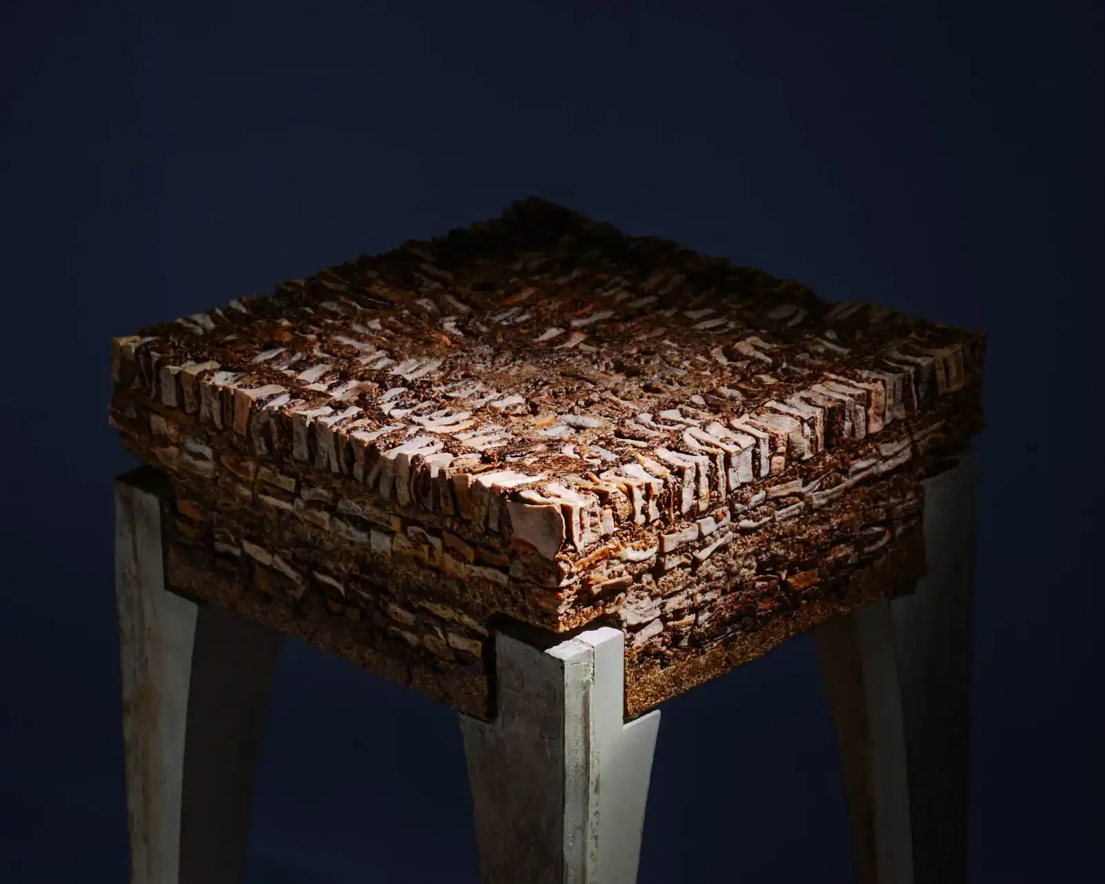 A square table made of stacked bricks supported by white wood legs, with a dark background.