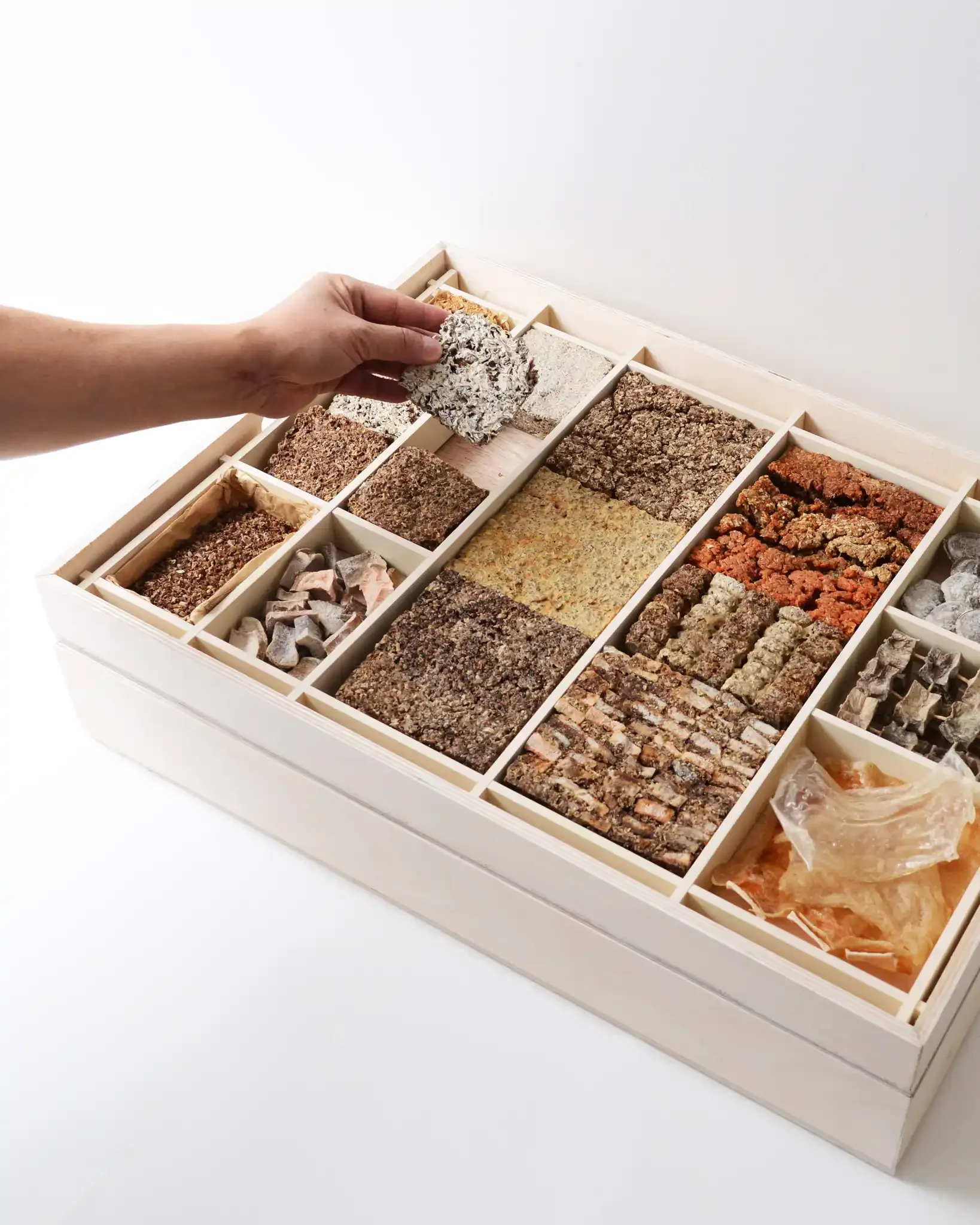 Hand lifting a piece of rocks from a compartment in a wooden display box filled with various types of rocks and minerals.