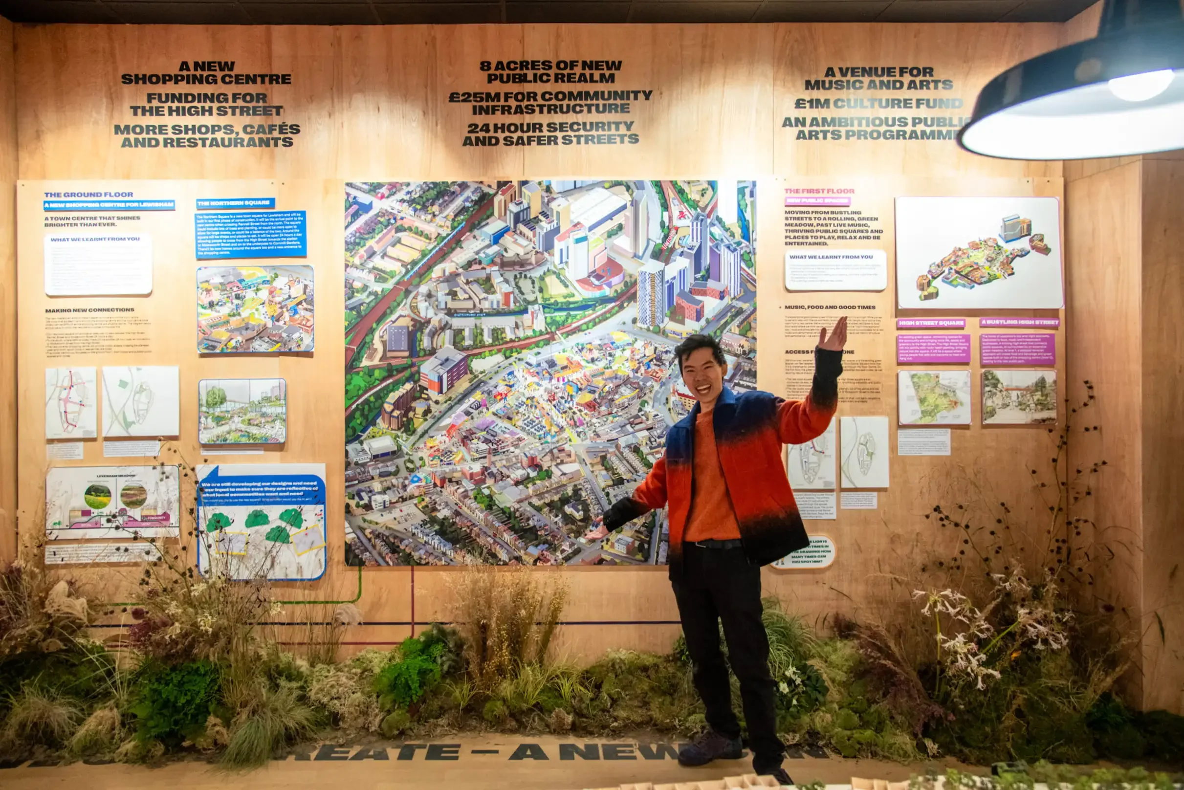 A smiling person standing in front of an informational display about a new urban development project for Lewisham Town Centre, with a large map and various sections of text about the plans for the area.