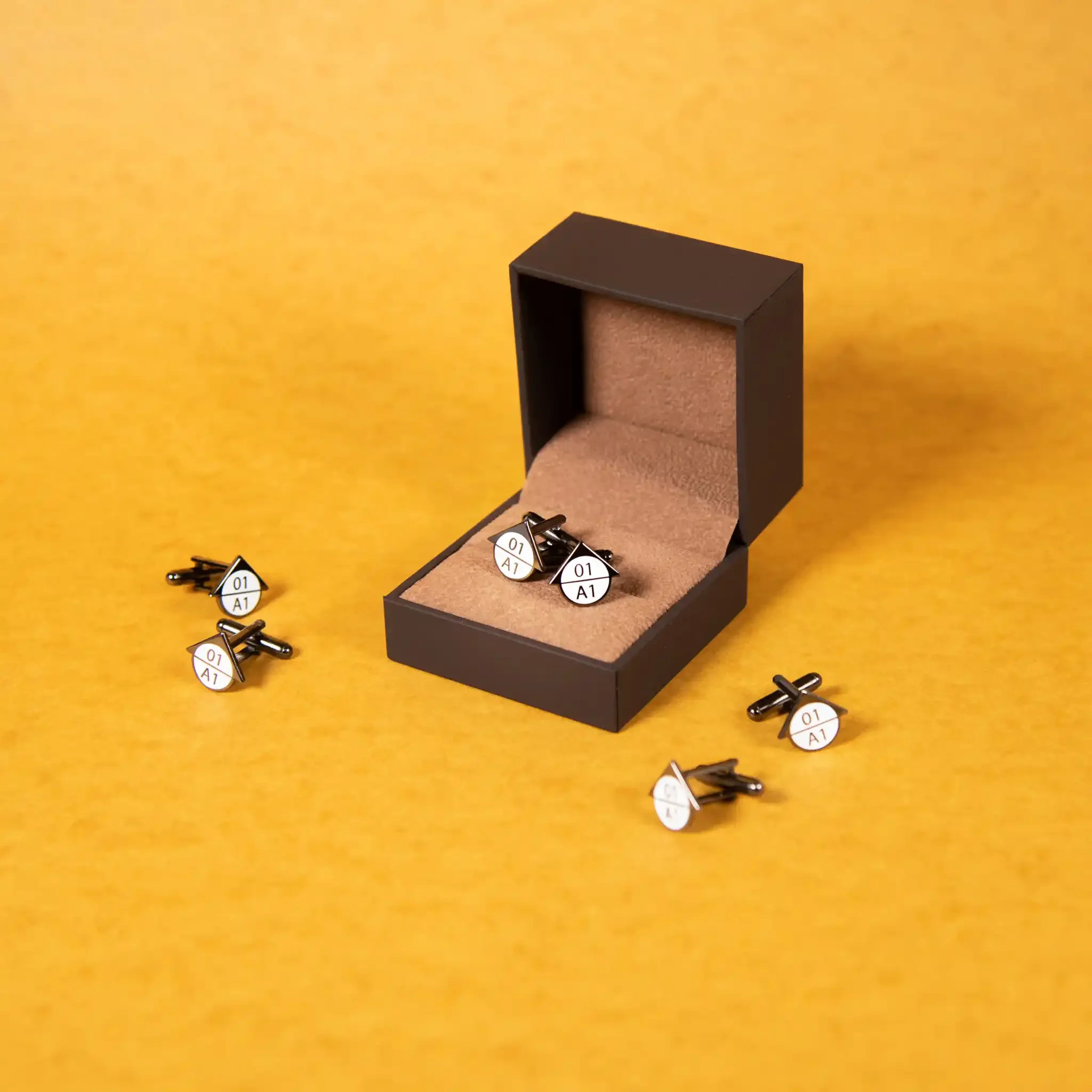 Black box with a velvet interior, containing small white and black circular objects labeled '01 A1,' some scattered outside the box on a yellow background.