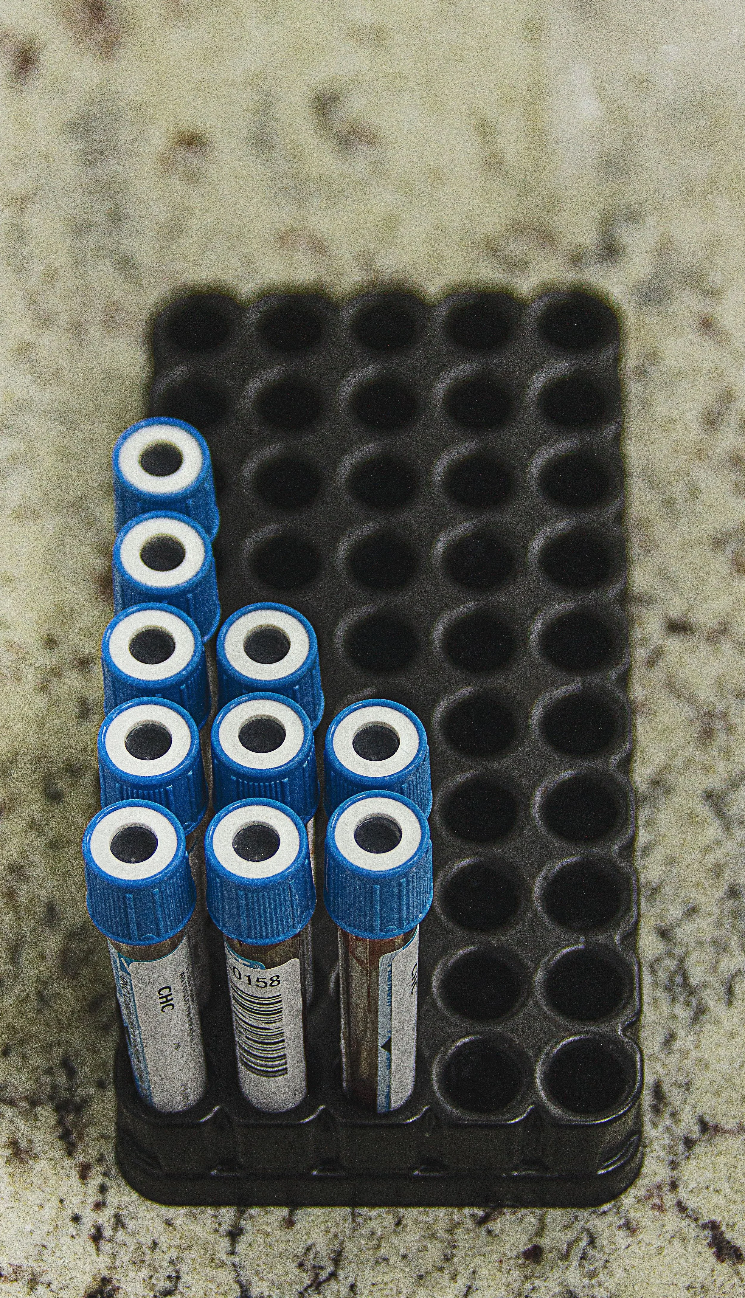 Six blue-capped markers in a black plastic case with circular slots, resting on a speckled countertop.