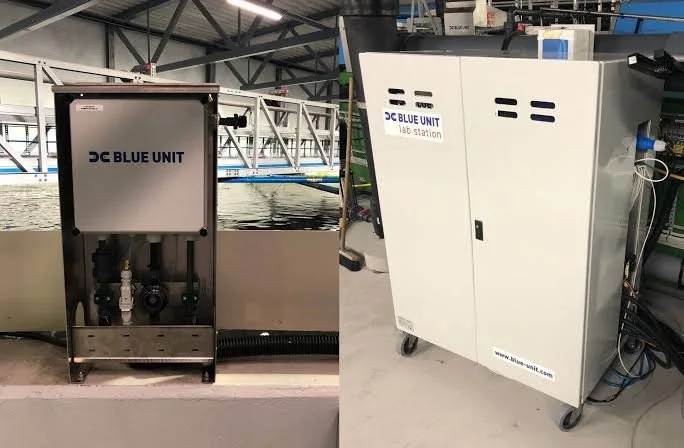 Industrial equipment labeled 'Blue Unit', consisting of a metal box with valves and wiring on the left, and a larger white cabinet on wheels with vents and cables on the right, in an industrial setting.