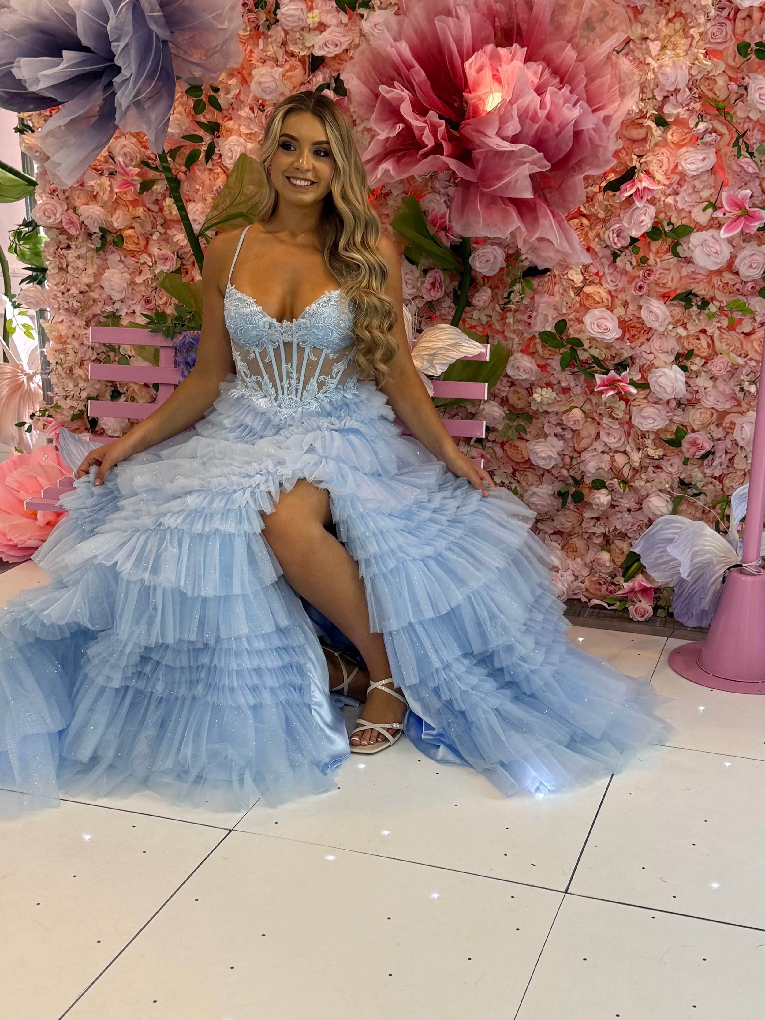 Girl wearing pale blue tiered tulle prom dress with corset top and front split, sitting on bench