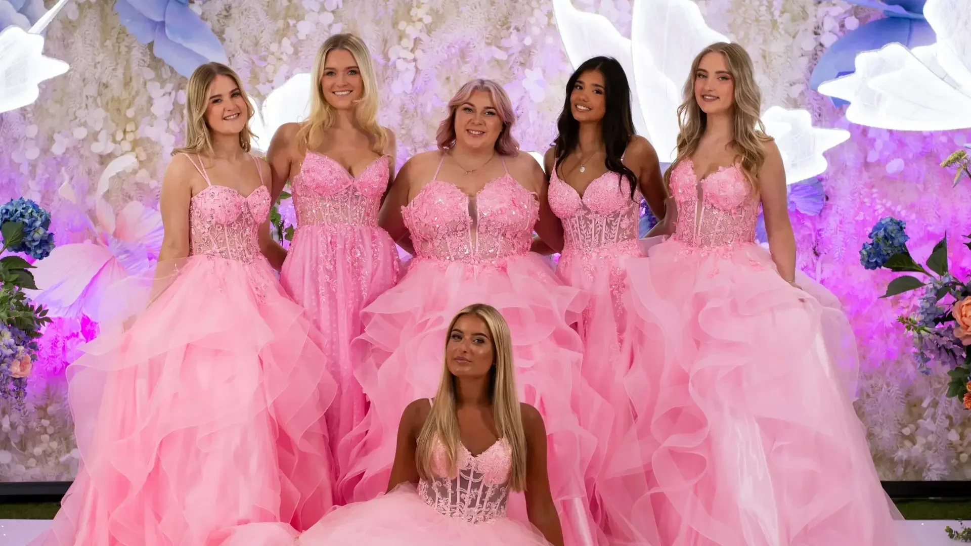 Group of six girls in matching pink corset prom dresses with tulle skirts at photo wall