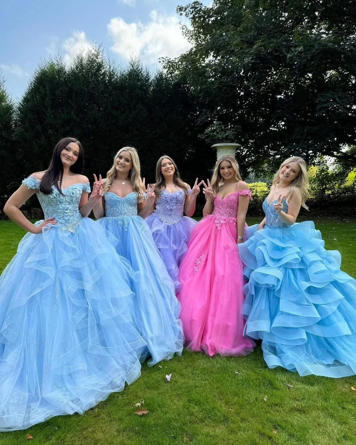 Five girls in pastel blue, lilac and pink prom ball gowns posing outdoors before prom night