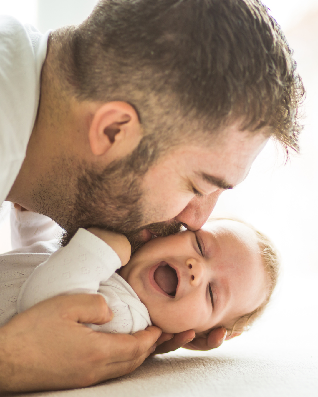 Vater küsst lächelnd schlafendes Baby auf der Nase.