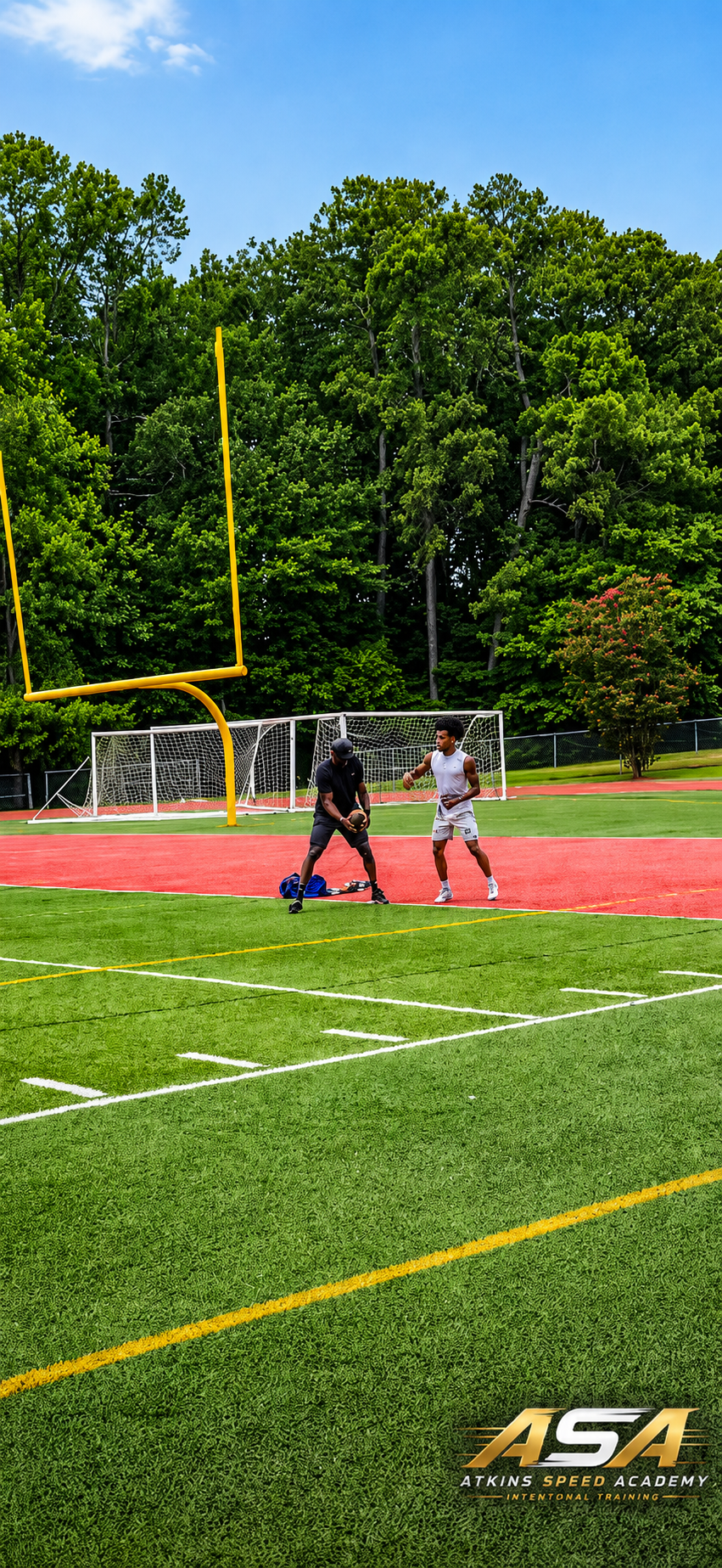 Two people training on a football field with goalposts, one person holding a football and the other possibly coaching or observing, with green trees and a blue sky in the background, and the logo 'ASA Atkins Speed Academy' in the bottom corner.