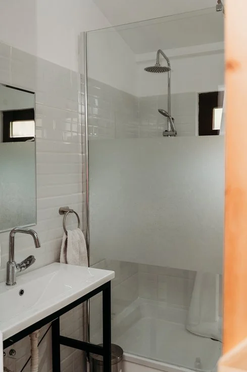 Bathroom with walk-in shower, small window, sink with a towel, and mirror.