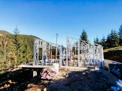 Construction site with steel framing for a building, surrounded by trees and a clear blue sky.