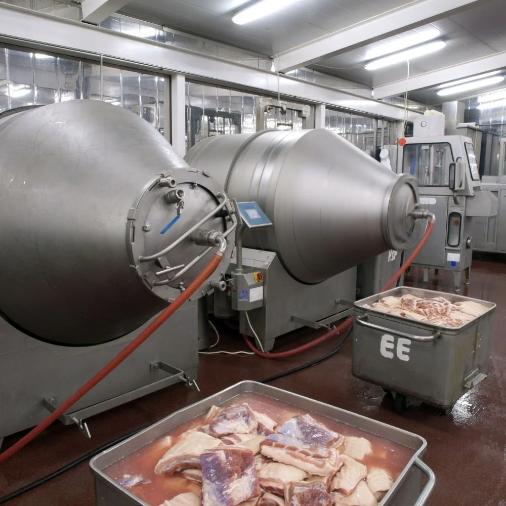 Industrial meat processing machine with trays of raw meat in a clean, bright facility.