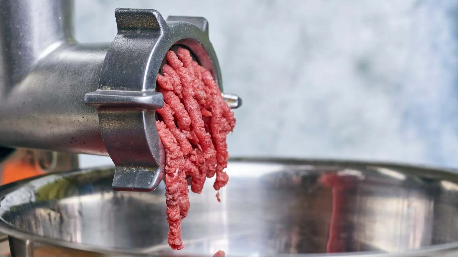 Ground meat being extruded from a meat grinder into a metal bowl.