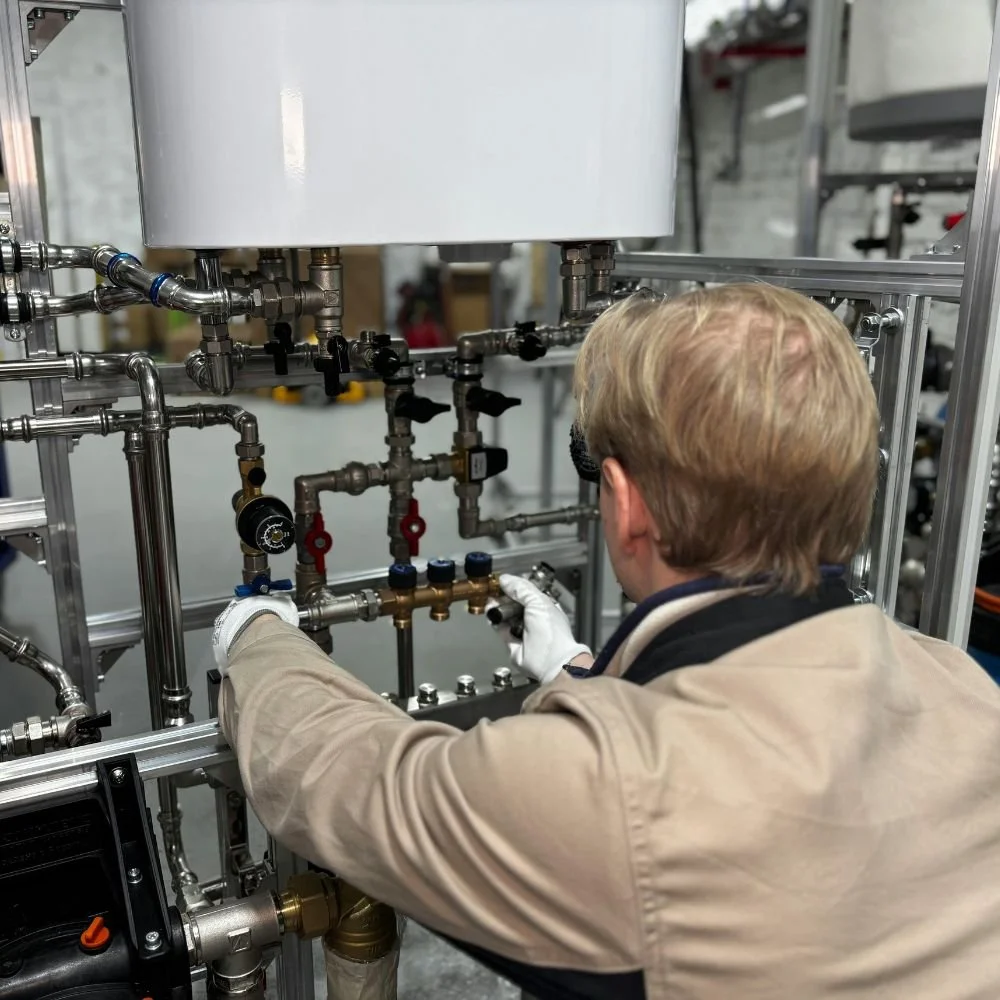 A worker inspecting or repairing pipes and valves in an industrial or laboratory setting.