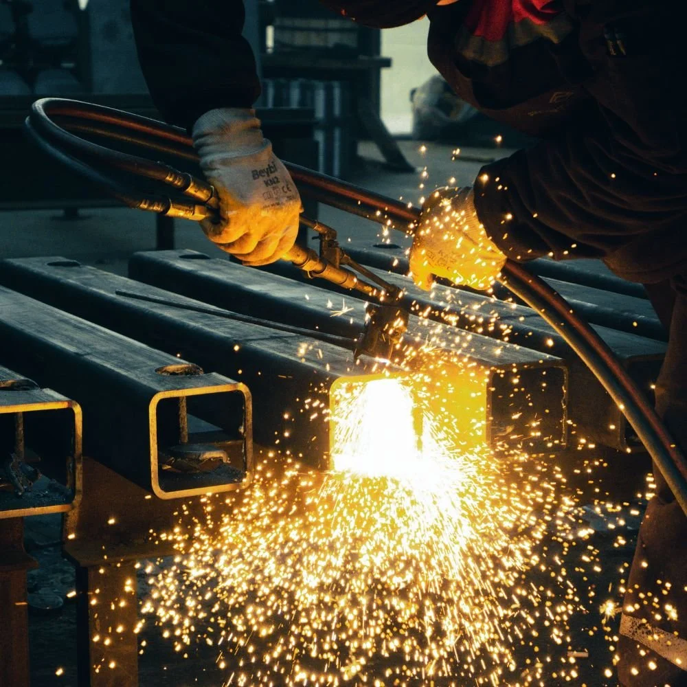 A worker welding metal beams while sparks fly in an industrial workshop.