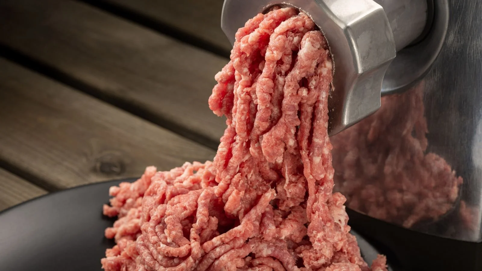 Close-up of ground beef being extruded from a meat grinder onto a black surface.