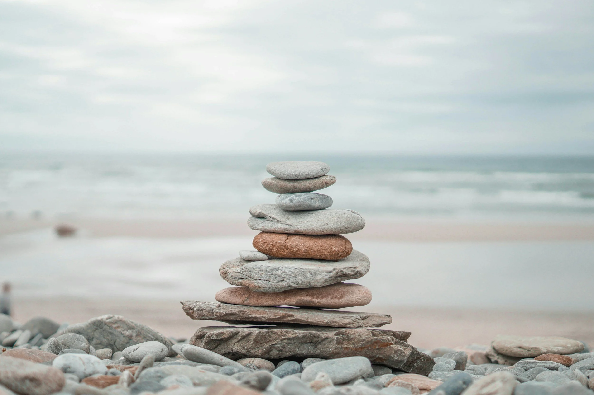 A stack of flat, smooth stones balanced on top of each other on a beach with cloudy sky and ocean in the background.