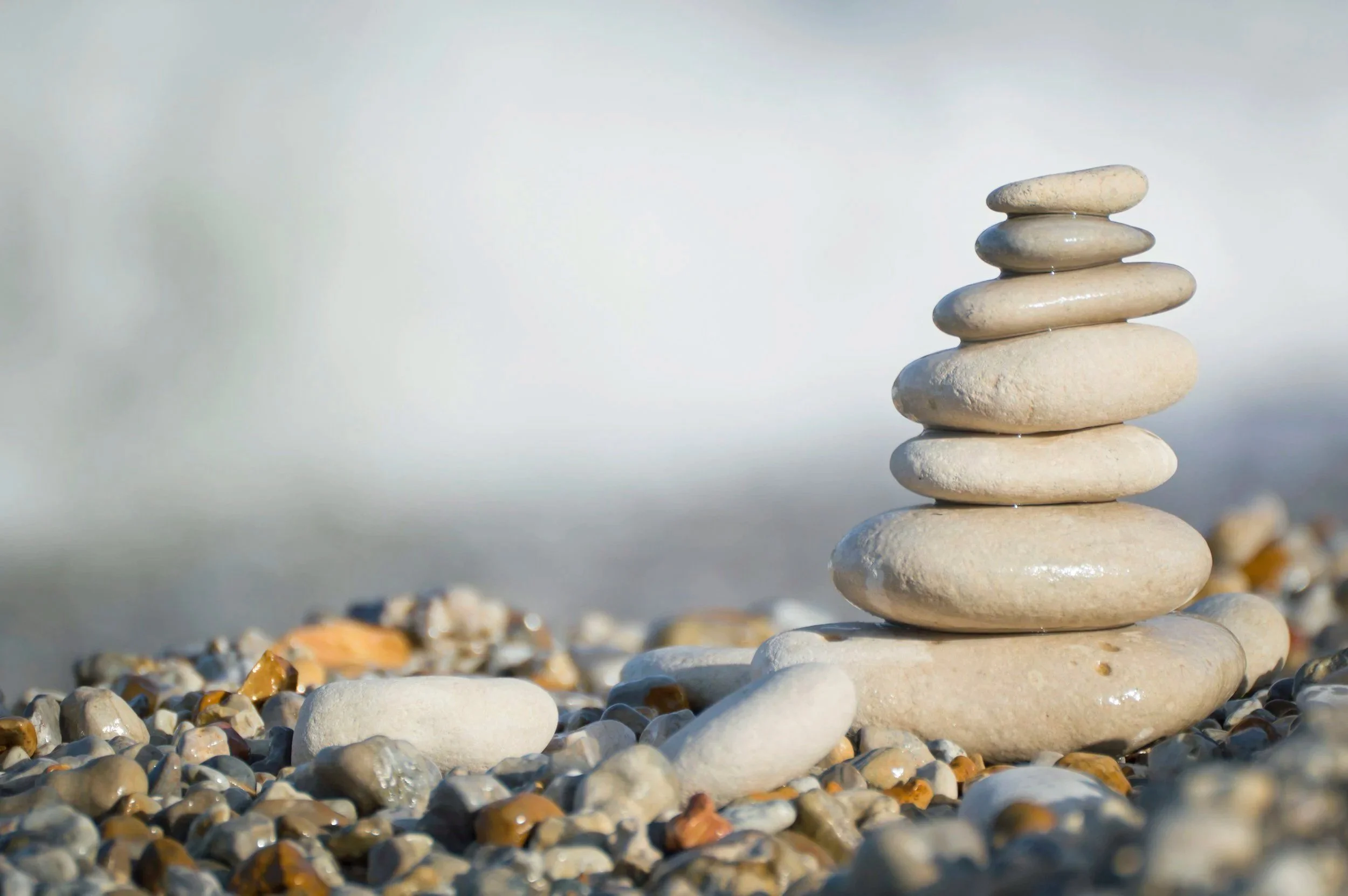 A neatly stacked formation of smooth, rounded white stones on a pebbly beach with calm water in the background.