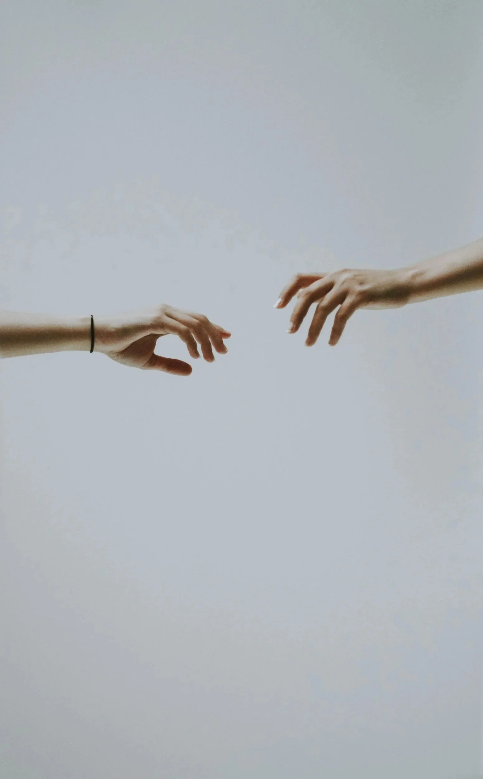 Two hands reaching towards each other against a plain background.
