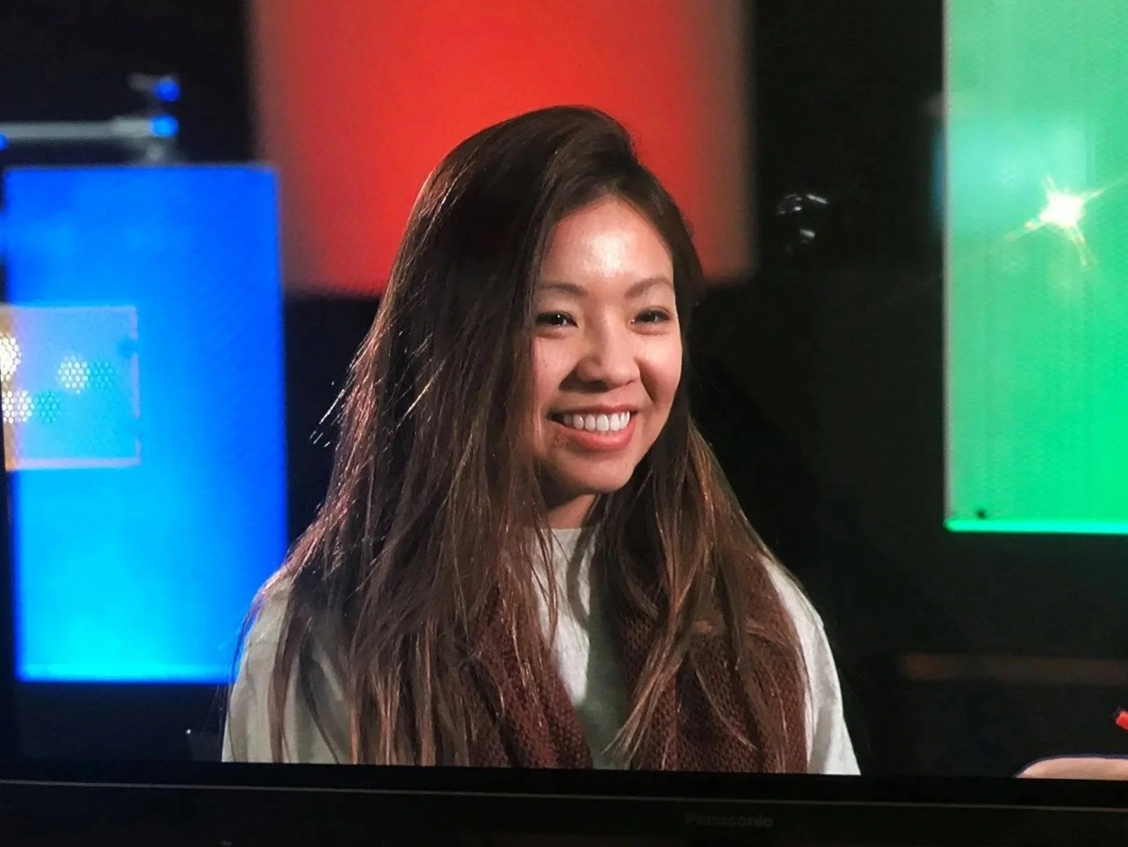 Susan Thao Sinclair | A smiling woman with long, dark hair in front of colorful digital screens.
