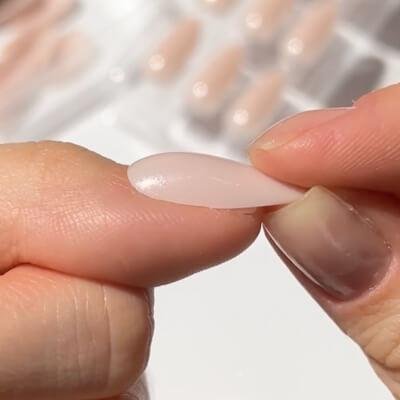 Close-up of a person sizing a press on nail on to their natural nail.