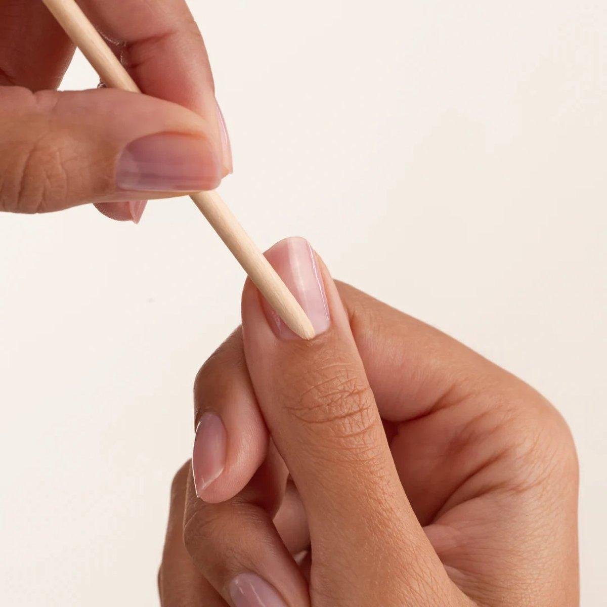 Person removing a press on nail with a wooden cuticle stick.
