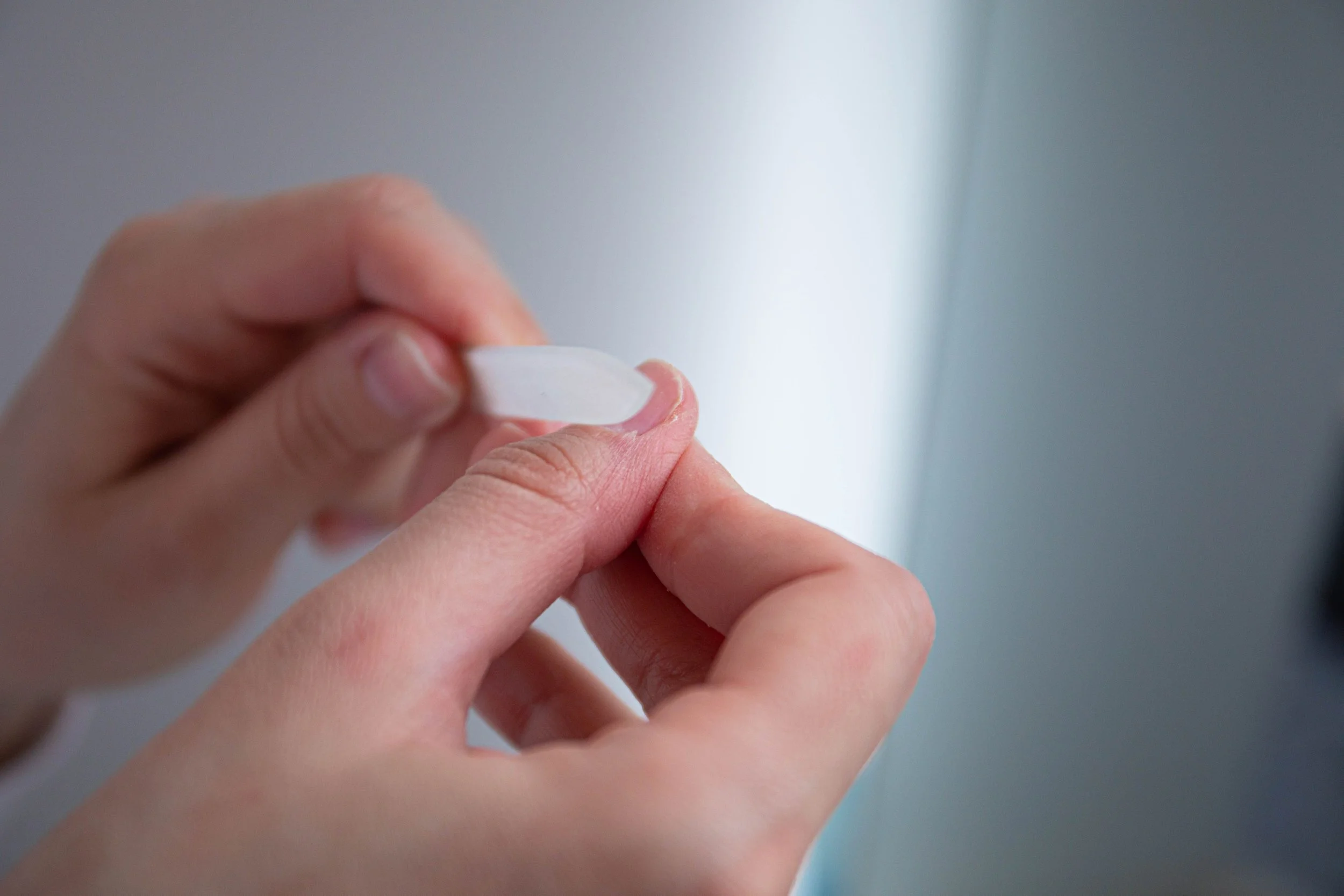 Close-up of a person's hands, buffing lightly on their nails using a nail buffing block/ file.