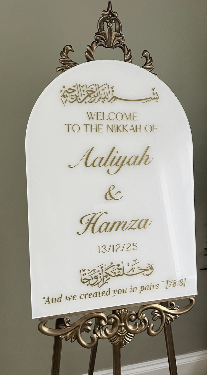 A decorative welcome sign with gold accents on a white background, saying "Welcome to the Nikkah of Aaliyah & Hamza" with the date 13/12/25, featuring Arabic calligraphy and a quote from the Quran.