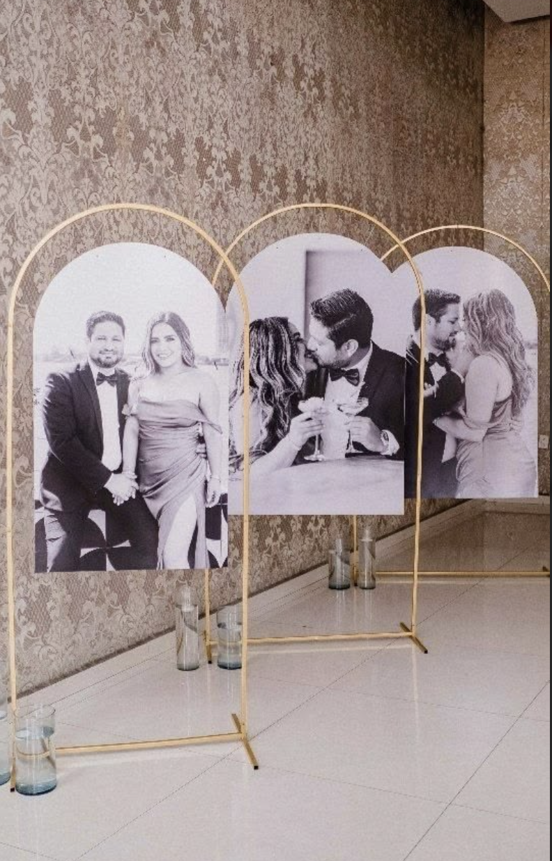 Three black and white framed photographs of couples in romantic settings, displayed on a decorative gold stand, with candles at the base.