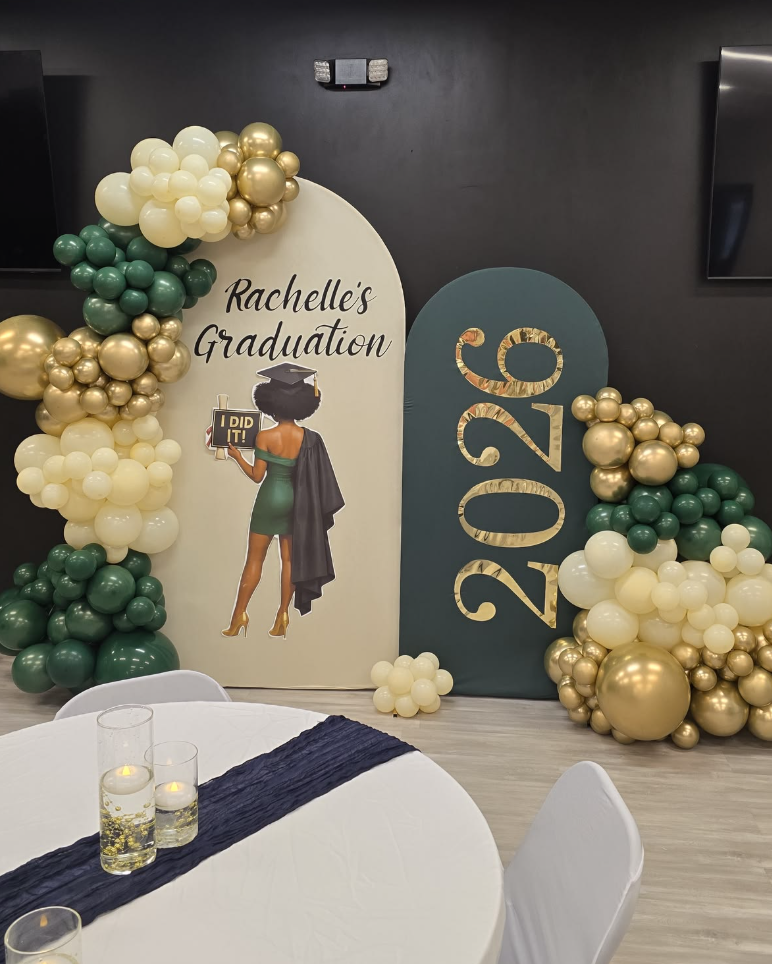 Decorative graduation celebration setup with balloons in white, gold, and green, a banner reading "Rachelle's Graduation," and large numbers "2022."