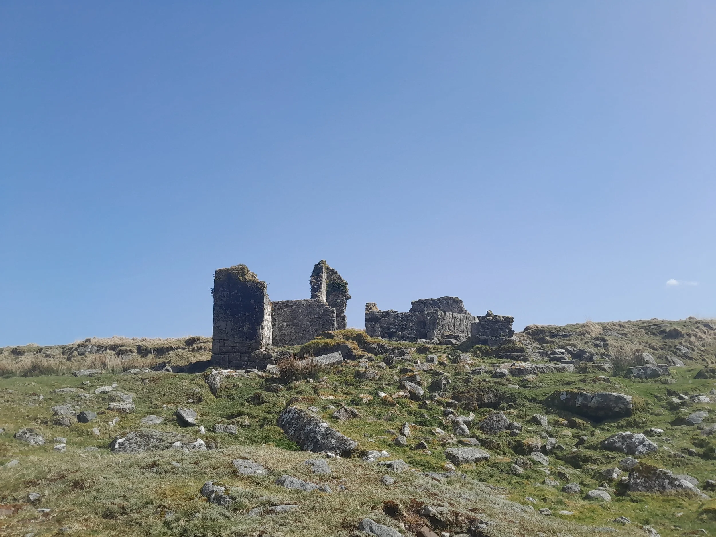 Ruins of an ancient stone structure on a grassy hillside under clear blue sky.